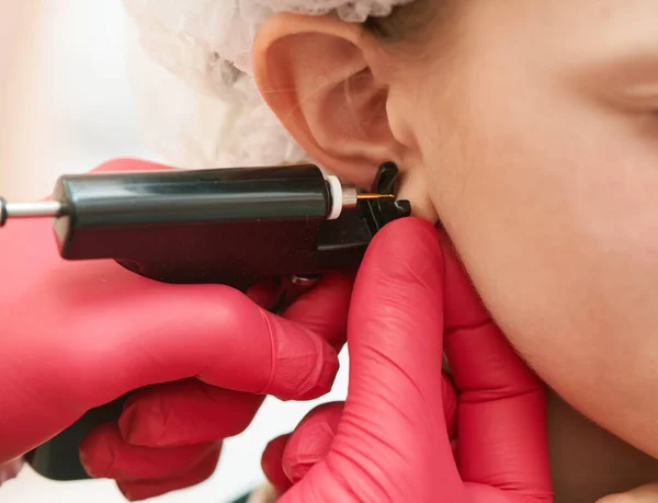 一名专业医务工作者在美容中心用特殊设备进行耳朵穿刺时的小女孩 — 图库照片