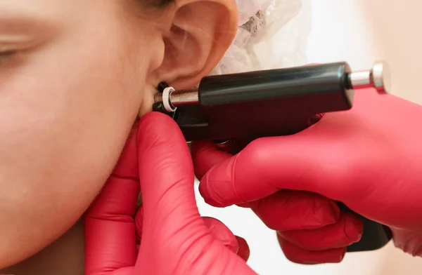 一名专业医务工作者在美容中心用特殊设备进行耳朵穿刺时的小女孩 — 图库照片
