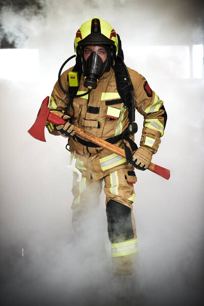 fireman with axe in protection wear at work walking through smoke.