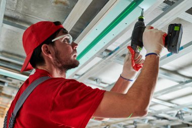 Alçıtaşı alçıtaşı kurulumu. Alçıpan evde çalışıyor. Müteahhit işçiler apartman geliştirme sırasında tavanda metal çerçeve tornavida