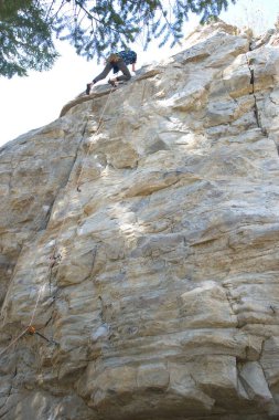 Back of male climber at top of climb showing rope path and sky clipart