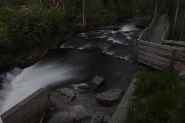 Akan dere suyu, sağ tarafında ahşap patika, ön ve arka planında yeşil yapraklar.