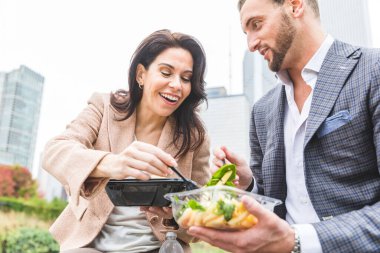 Chicago Park'ta öğle yemeği iş adamları. Makarna ve salata öğle tatilinde yeme, smart casual elbiseler giymiş kadın ve erkek. Arka plan üzerinde şehir gökdelenler