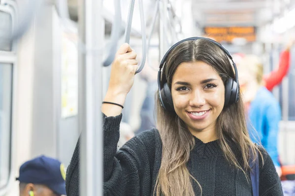 シカゴの地下鉄で幸せな多人種の少女の肖像画 市内の公共交通機関を利用しながら カメラを見てヘッドフォンで音楽を聴く若い女性 — ストック写真