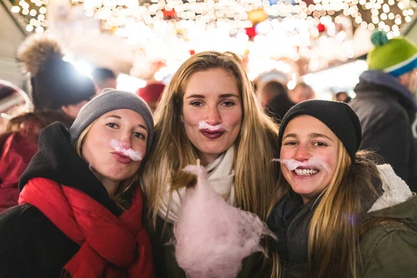 在圣诞市场上吃棉花糖和做假胡子的女孩 三位快乐的年轻女性享受着在一起的时光和快乐 — 图库照片