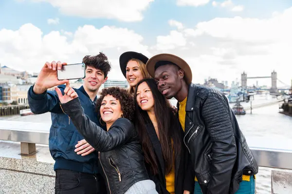 ロンドンで一緒にセルフィーを取る友人のグループ バックグラウンドでタワーブリッジと写真を撮る旅行で多種多様な人種間の友人 旅行とライフスタイル ロイヤリティフリーのストック写真