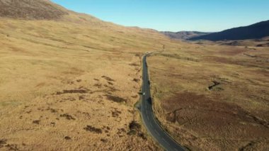 Snowdonia 'nın Galler bölgesinde geniş ve ıssız bir vadiden geçen kırsal bir yoldaki arabaların hava görüntüsü seyahat ve ulaşım kavramlarına sahip.