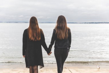 İki kadının el ele tutuşması, sakin bir göl ya da nehir kenarındaki mesafeye bakması - iki kadın ya da göl kenarında el ele tutuşan arkadaşlar