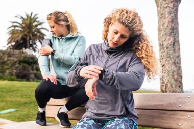 Antrenmandan sonra akıllı saat ve telefonu kontrol eden kadınlar - Porto 'da eğitim gören iki genç kadın, sağlıklı yaşam tarzı ve spor kavramları - teknoloji ve giyilebilir cihazlar