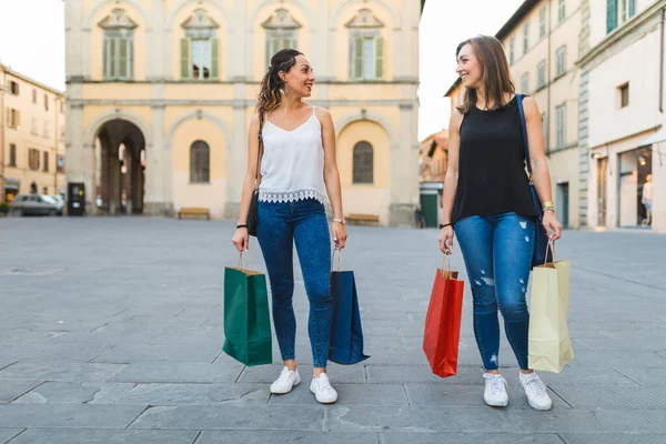 Two women strolling through city streets with colorful shopping bags - Shopping best friends enjoying retail therapy in Italy