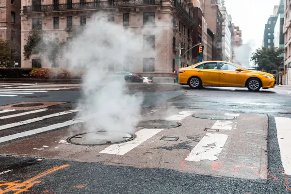 在纽约 城市街道充满了蒸汽 从一个人孔里冒出 一辆出租车在行驶 城市里有黄色出租车的蒸汽街场景 — 图库照片