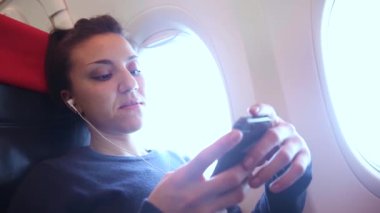 Uçakta akıllı telefonuyla müzik dinleyen bir kadın seyahat ve teknoloji kavramları, kulaklık takan genç bir kadın.