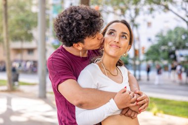 Mutlu çift sarılıyor ve öpüşüyor - bir adam kız arkadaşını arkadan kucaklıyor ve yanağından öpüyor - sevgi ve ilgi kavramları