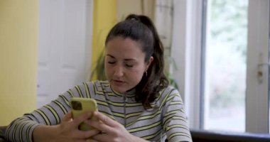 Otantik çekim kadını koltukta cep telefonu kullanıyor ve başarıyı veya zaferi online olarak kutluyor - evde teknoloji ve sosyal medya kavramlarıyla yaşam tarzı