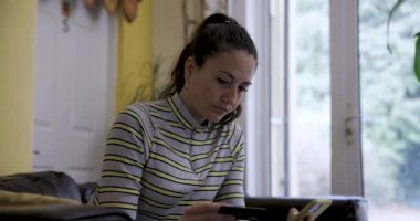 Kanepede cep telefonu ve kredi kartı olan genç bir kadın çevrimiçi alışveriş yapıyor ya da tatil rezervasyonları yaptırıyor - teknoloji ve ev bankacılığı kavramlarıyla evde yaşam tarzı