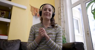 Evden çalışan bir kadının uzaktan görüşmesinde kulaklık takan ve kamerayla konuşan gülümseyen genç bir kadın.