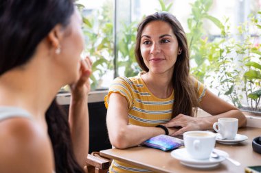 Two women best friends enjoying a coffee break in a cafe bar - Caucasian and asian women together in Barcelona, friendship, multicultural city and lifestyle