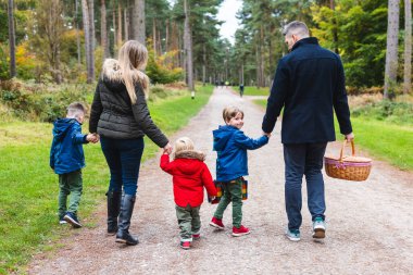 Family walks happily in a peaceful forest during autumn, holding hands and enjoying nature together clipart