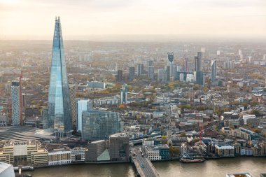 Londra ufuk çizgisinin havadan görünüşü gökdelenleri, çevresindeki binaları Thames nehri ve bulutlu gökyüzünü aydınlatıyor.