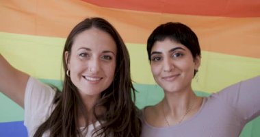 Mutlu kız arkadaş lezbiyen çiftin arka planda gökkuşağı bayrağı tutarken ve eşcinsel evli eşcinsel çift olarak mutluluğu gösterirken otantik bir çekimi.