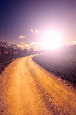 Gün batımında Toskana bahar tarlaları arasında dönen toprak yol..