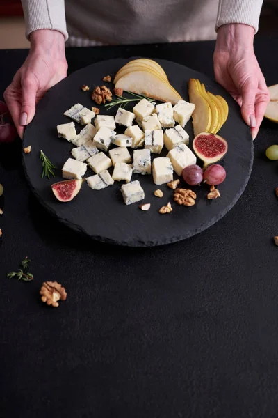 Woman puts stone serving board with Sliced Traditional Italian Gorgonzola cheese on a table.