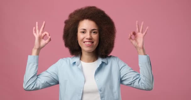 アフロヘアスタイル ノドルとピンクのスタジオの背景に立って指でOkサインハンドジェスチャーを示す陽気な若いアフリカ系アメリカ人の女の子 Dci 二重スローモーション — ストック動画