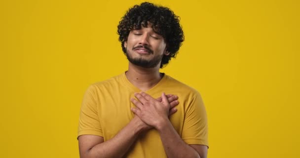 感激的 感激的 感激的 感激的 感激的印度年轻人手拉手靠近胸部 在橙色工作室的背景下 触动了心脏 Dci 2X慢动作 — 图库视频影像