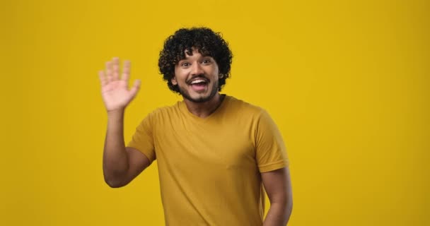 年轻的印地安人挥手打招呼欢迎某人站在橙色工作室的背景上表达积极的情感 Dci 2X慢动作 — 图库视频影像