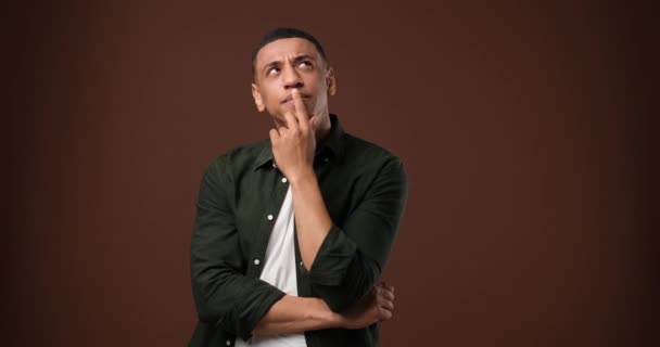若いアフリカ系アメリカ人男性の思考と茶色のスタジオの背景の上に立って検索のクローズアップ肖像画 Dci 二重スローモーション — ストック動画