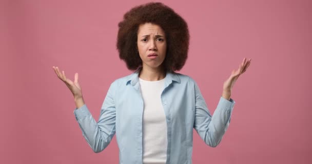 感情的に理解できないアフリカ系アメリカ人女性が肩をすくめ 手を上げてピンクのスタジオの背景に立つ理由を尋ねる Dci 二重スローモーション — ストック動画