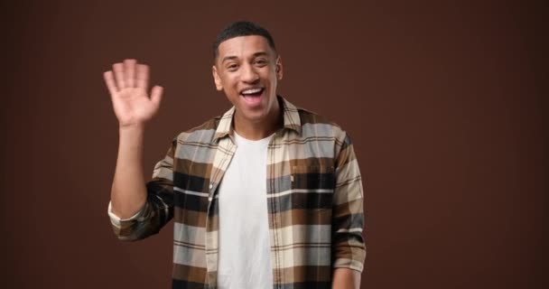 年轻的非洲裔美国人挥手打招呼 欢迎某人站在棕色工作室的背景上表达积极的情感 Dci 2X慢动作 — 图库视频影像