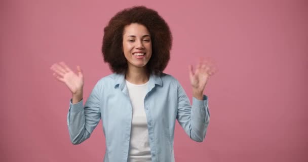 快乐友善的年轻非洲裔美国女人挥手打招呼 欢迎有好客表情的人站在粉红的背景上表达积极的情感 Dci 2X慢动作 — 图库视频影像