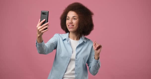 快乐的非洲裔美国女人 有手机视频通话 挥挥手打招呼 站在粉红的背景下打招呼 Dci 2X慢动作 — 图库视频影像