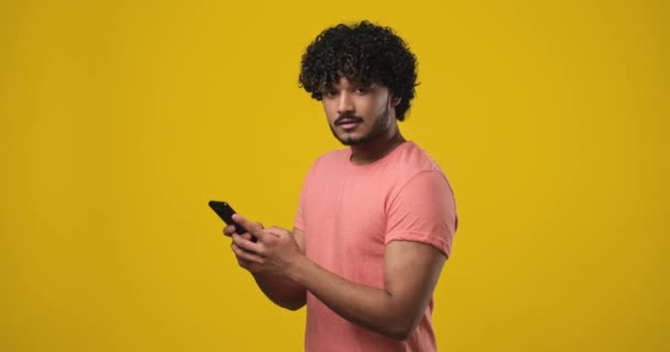 若い笑顔の普及したインド人男性を使用して携帯電話の入力Smsメッセージを脇にオレンジのスタジオの背景に検索します Dci 二重スローモーション — ストック動画