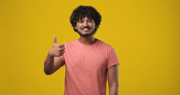 若い幸せな笑みを浮かべてインド人男性ジェスチャーオレンジのスタジオの背景に孤立立ってのような親指を表示します Dci 二重スローモーション — ストック動画