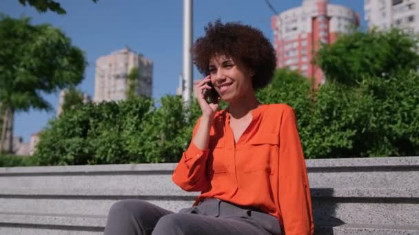 Ung Afroamerikansk Kvinna Med Lockigt Hår Talar Mobiltelefon Sitter Utomhus — Stockvideo