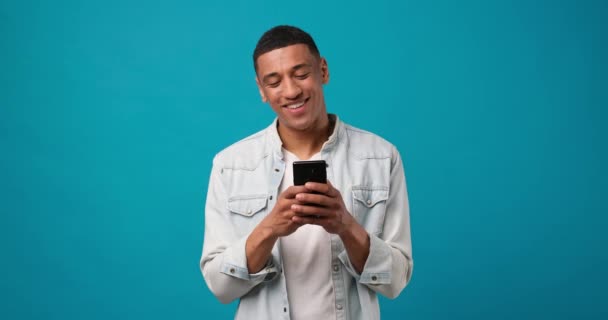 Młody Uśmiechnięty Afrykański Amerykanin Używający Telefonu Komórkowego Wpisujący Sms Patrząc — Wideo stockowe