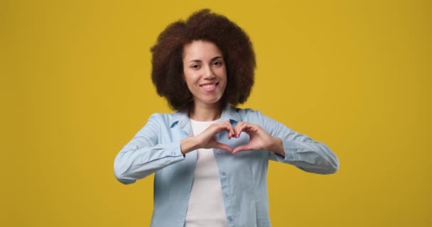 快乐的年轻非洲裔美国女人在橙色工作室的背景下表现出爱心之手的姿态 Dci 2X慢动作 — 图库视频影像