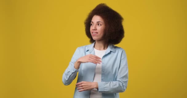 オレンジ色のスタジオの背景に隔離された手で広告や製品の配置のための空のモックアップスペースに脇を示す若いアフリカ系アメリカ人女性 Dci 二重スローモーション — ストック動画