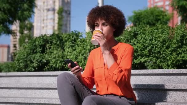 Ung Afroamerikansk Kvinna Med Lockigt Hår Håller Smartphone Och Kopp — Stockvideo