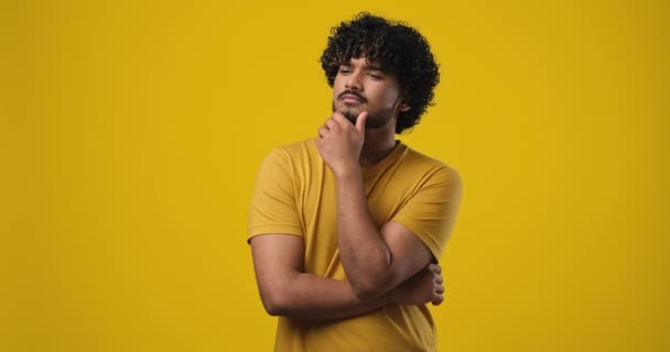 オレンジ色のスタジオの背景の上に立って顎の近くに手で考えている普及した若いインド人男性 Dci 二重スローモーション — ストック動画