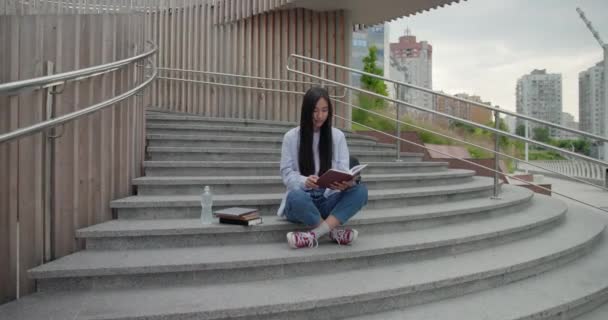 大学のコンセプトの教育 屋外でステップに座っている間 若い女性の読書ノートブック — ストック動画