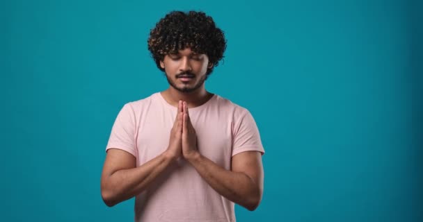 青いスタジオの背景に隔離された立場で目を閉じて祈る若いインド人男性 Dci 二重スローモーション — ストック動画