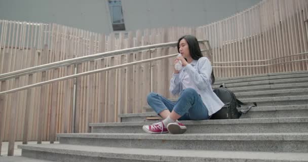 Genç Asyalı Kız Öğrenci Dışarıda Merdivenlerde Otururken Içiyor — Stok video