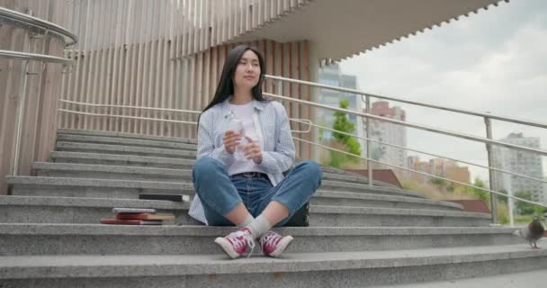 Genç Asyalı Kız Öğrenci Dışarıda Merdivenlerde Otururken Elinde Bir Şişe — Stok video