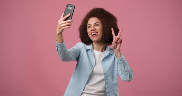 청바지 셔츠를 아메리카계 미국인 분홍색 스튜디오 배경으로 스마트폰으로 셀피를 만들고 — 비디오