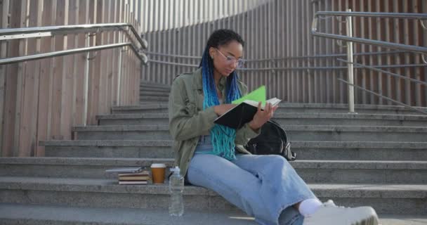 大学のコンセプトの教育 屋外でステップに座っている間 若い女性の読書ノートブック — ストック動画