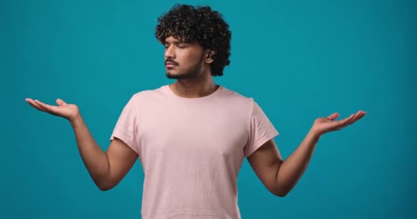 青いスタジオの背景に隔離された手で広告や製品配置のための空のモックアップスペースを脇に示す若いインドの男 Dciについて スローモーション — ストック動画