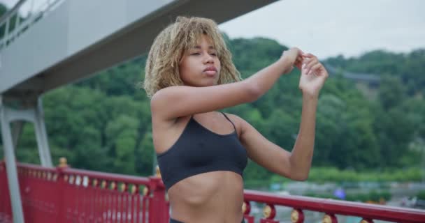 街の橋でジョギングする前に暖かく伸びる若いアフリカ系アメリカ人女性にフィット — ストック動画